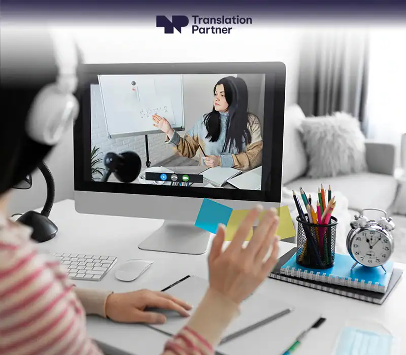 Person in online class with Translation Partner logo on screen and desk supplies.