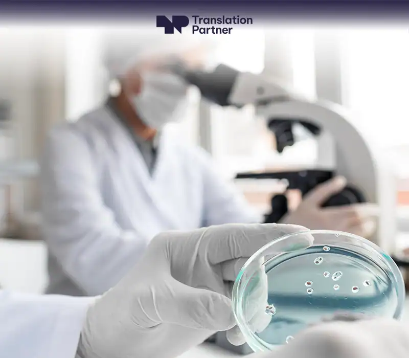 A gloved hand holds a petri dish in a lab, with a scientist using a microscope in the background, and the Translation Partner logo.