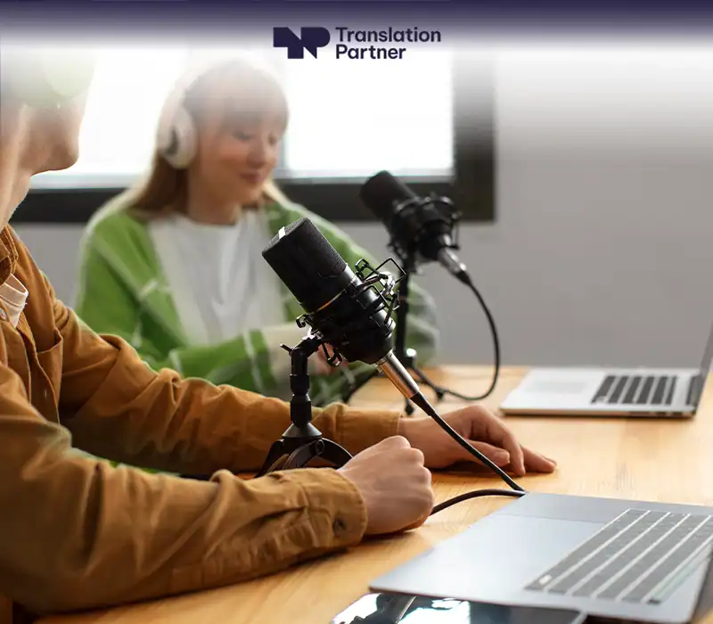 Two podcasters recording with microphones and laptops, "Translation Partner" logo visible.