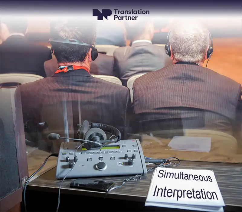 Simultaneous interpretation booth with equipment and Translation Partner logo.