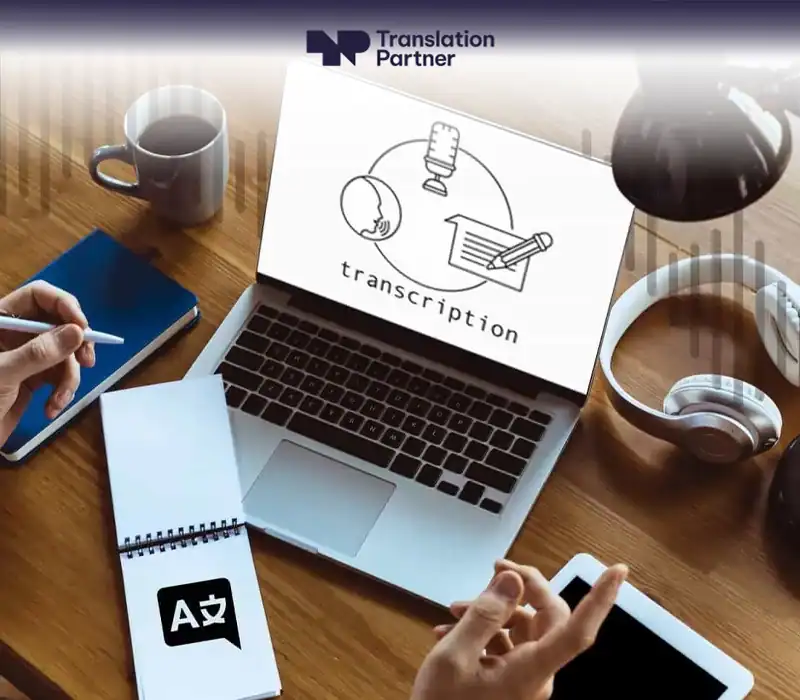 Transcription services workspace with laptop, notebook, headphones, and Translation Partner.